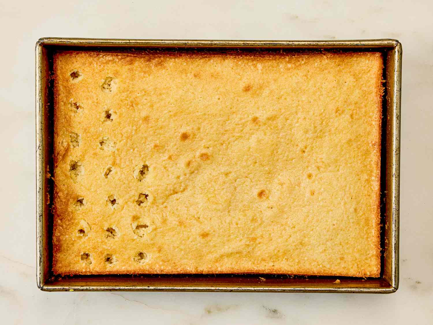 A rectangular baked cake in a pan with a series of holes poked into one corner