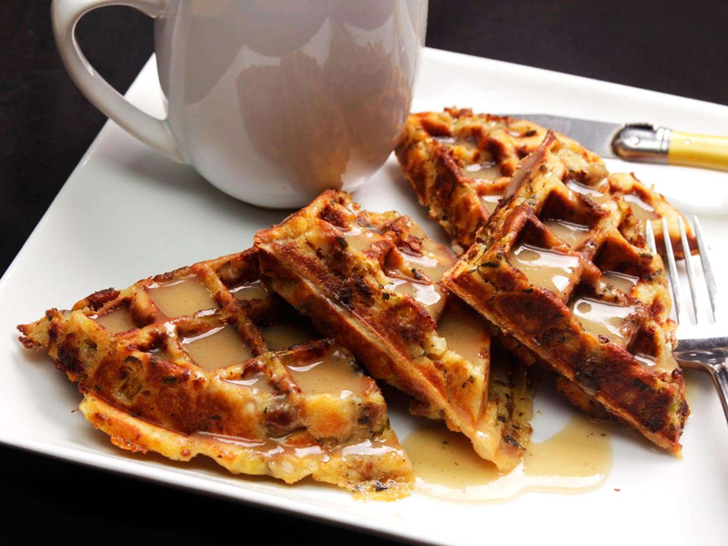 Cooked stuffing waffle on a white plate, doused with gravy syrup.