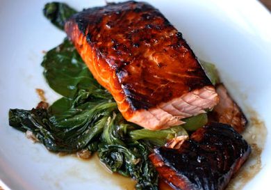 Teriyaki-glazed salmon on a bed of wilted bok choy on a white serving dish.