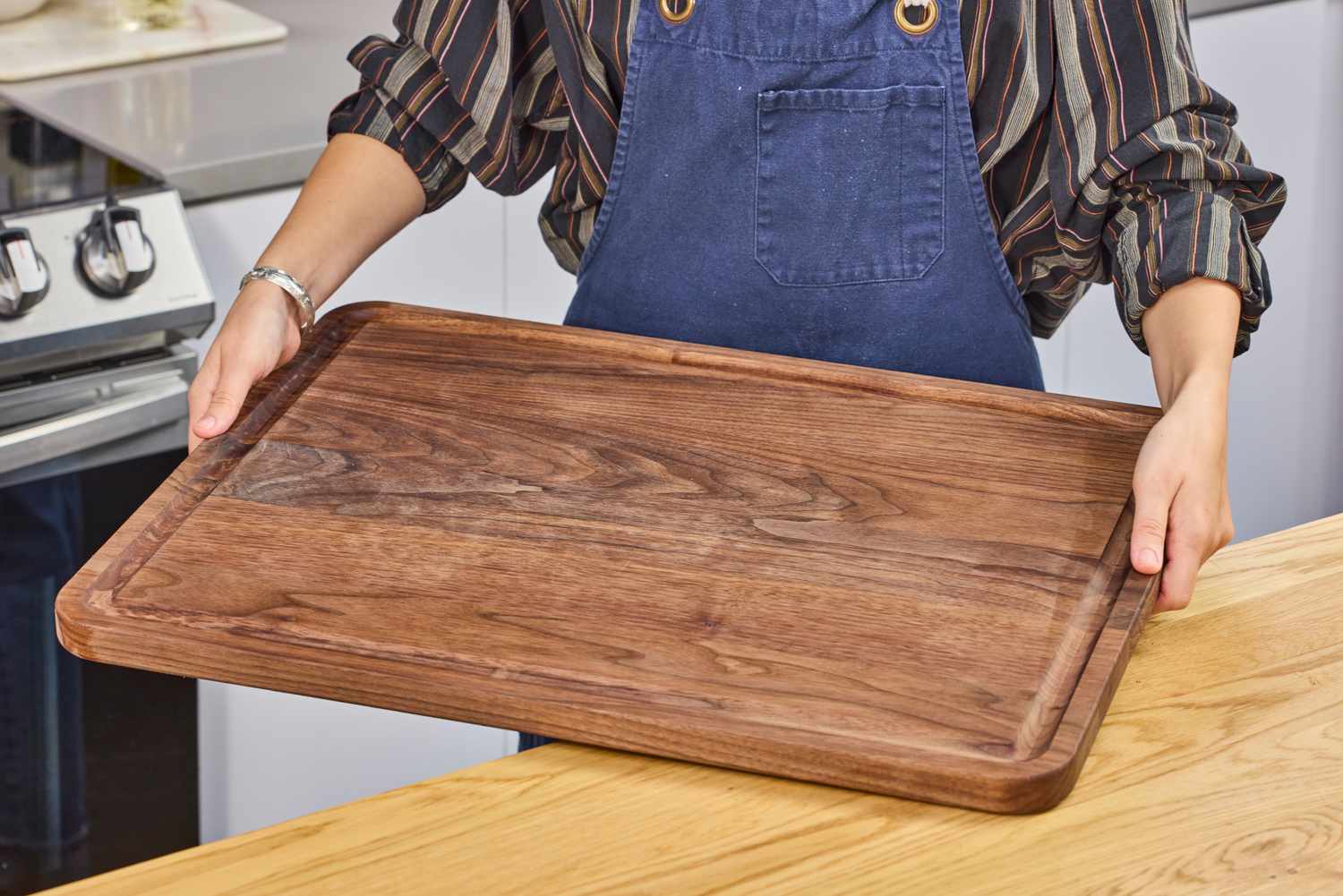 A person holding a Virginia Boys Kitchens Walnut Wood Cutting Board in a kitchen setting