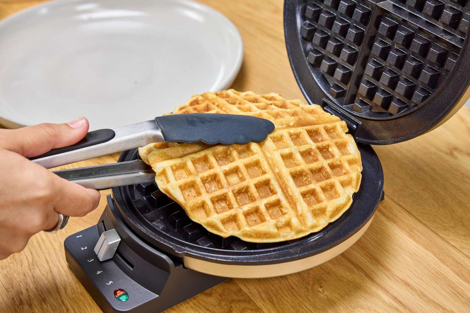 A person cooks a waffle in the Cuisinart WMR-CANAS Round Classic Waffle Maker