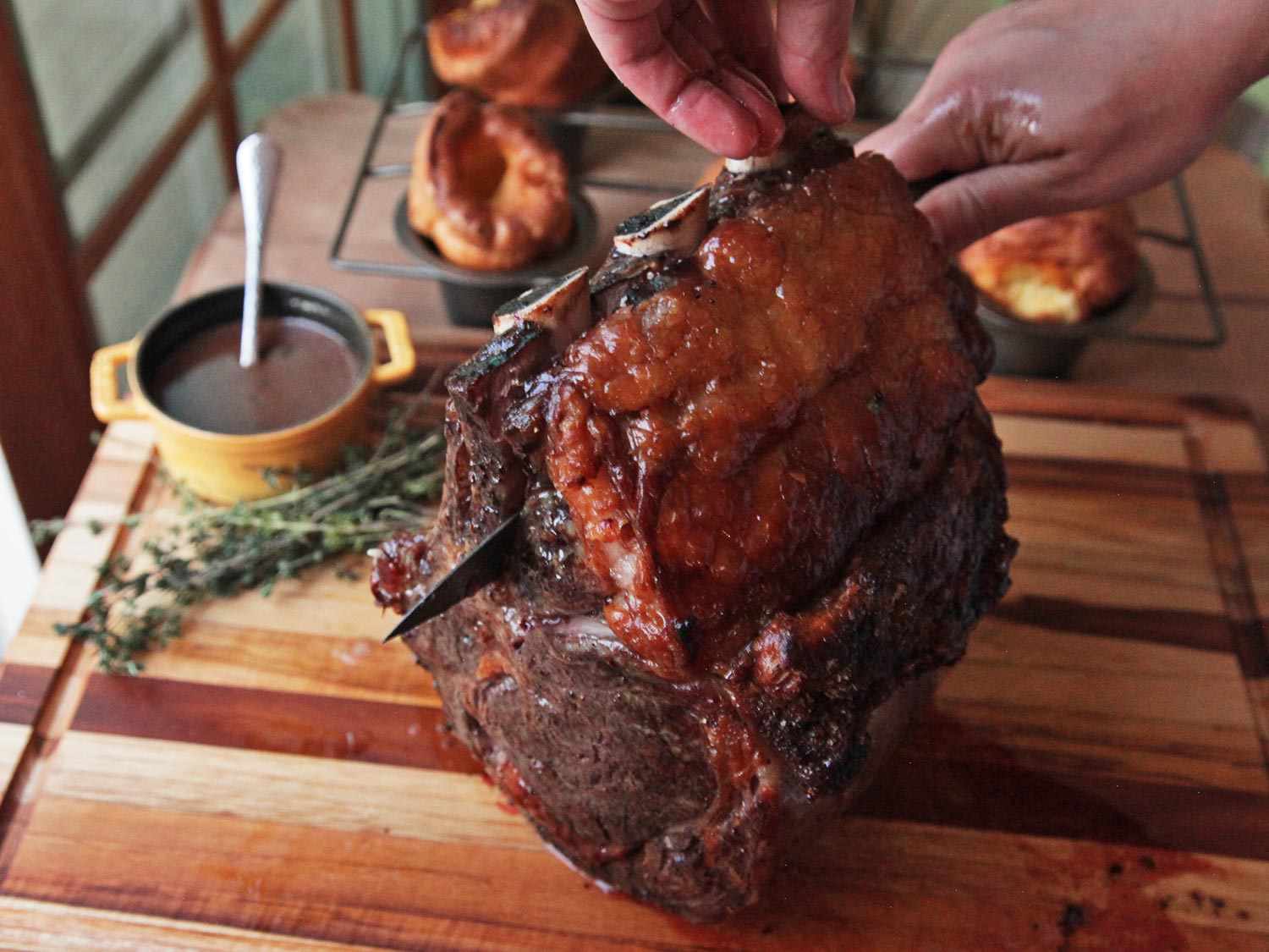 A roasted prime rib is propped up on a cutting board so that the rib bones can be cut free.