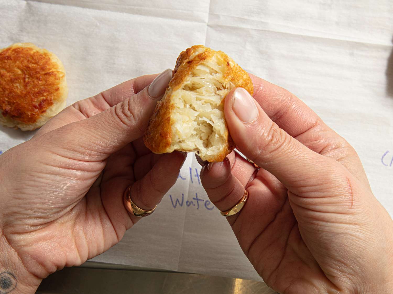 Hands breaking apart a cooked potato patty over parchment paper
