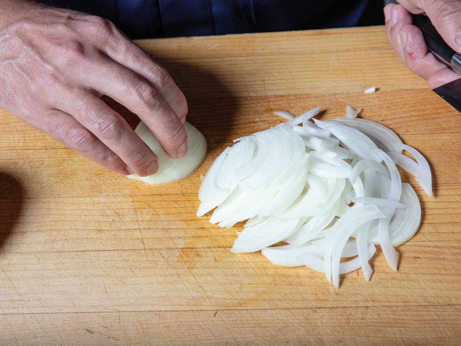 Pile of onions sliced pole to pole on a cutting board.