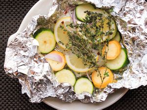 Overhead shot of green and yellow zucchini slices, sliced red onion, and thyme sprigs layered over cod in an open foil packet 