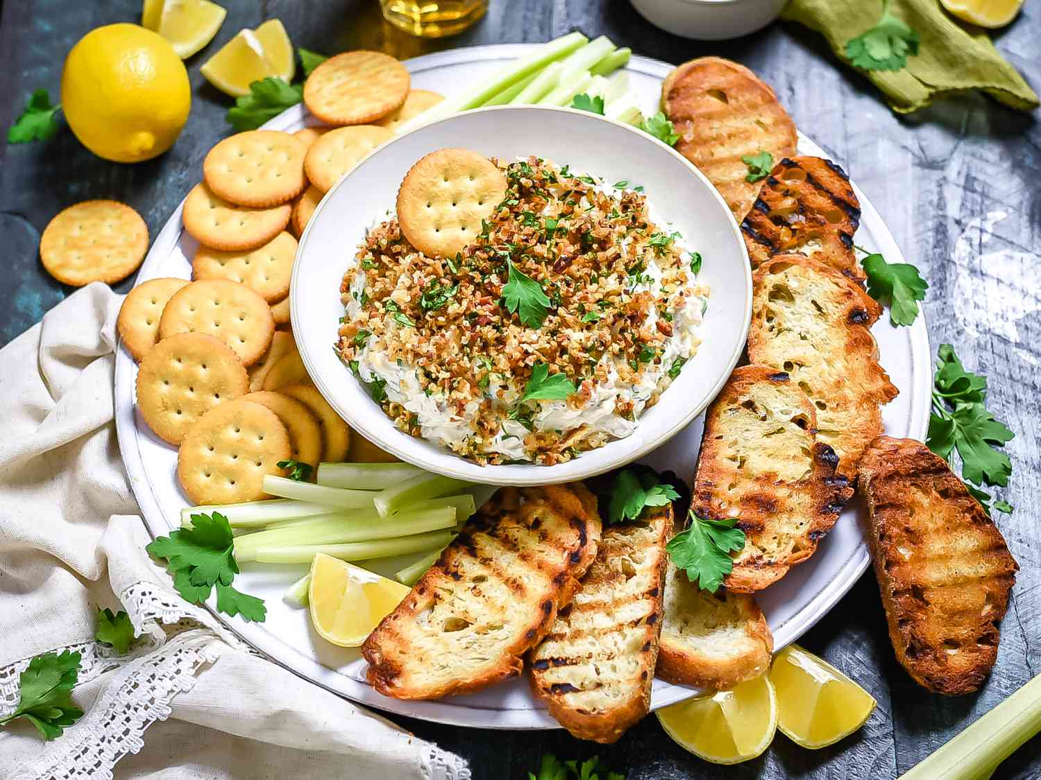Clams Casino Dip plattered with crackers, grilled crostini, celery sticks, and lemon wedges