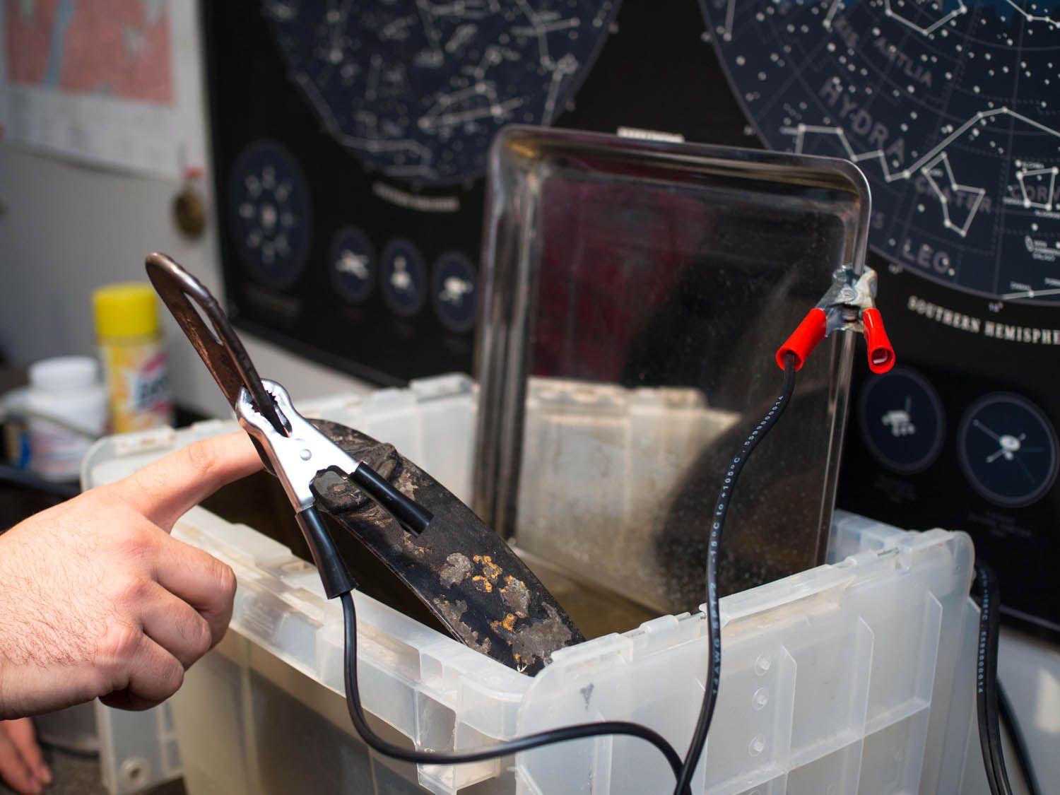 A cast iron skillet and a baking sheet connected to charging cables and placed in a water bath.