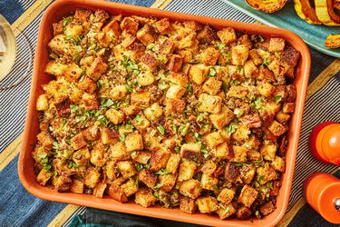 sausage and sage stuffing in orange baking dish, on a thanksgiving table, with roasted squash to the side. 