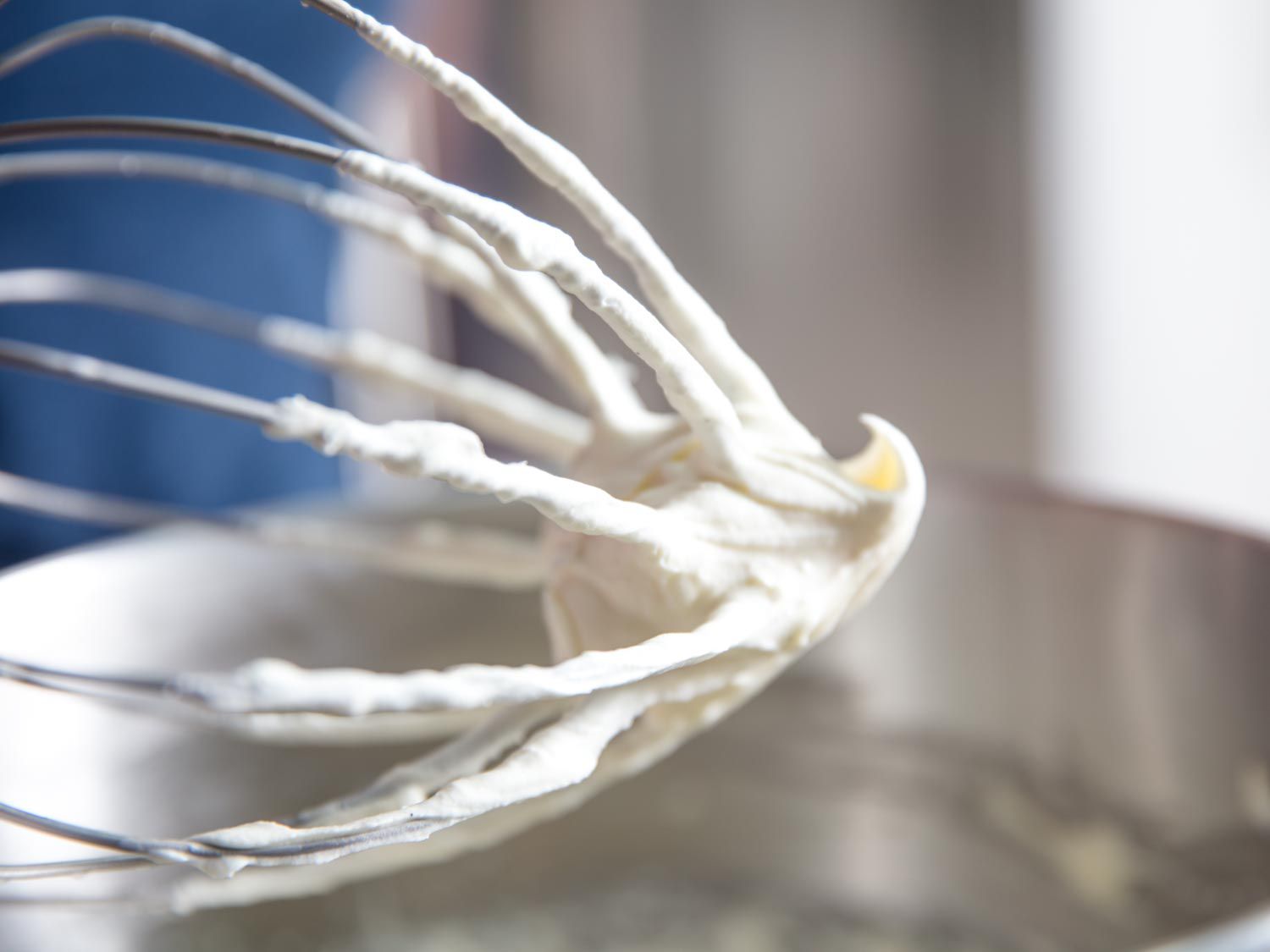 Close-up of the whisk attachment for a stand mixer. The lower half of the tines are coated in cheesecake filling.