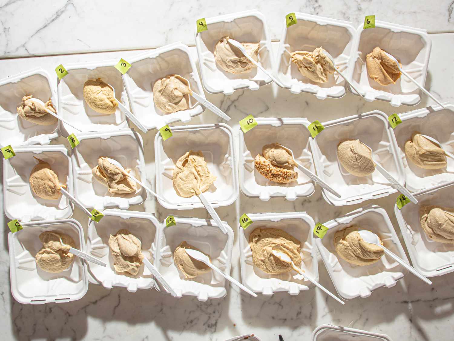 A selection of multiple containers with hummus samples for a taste test, each labeled with tags