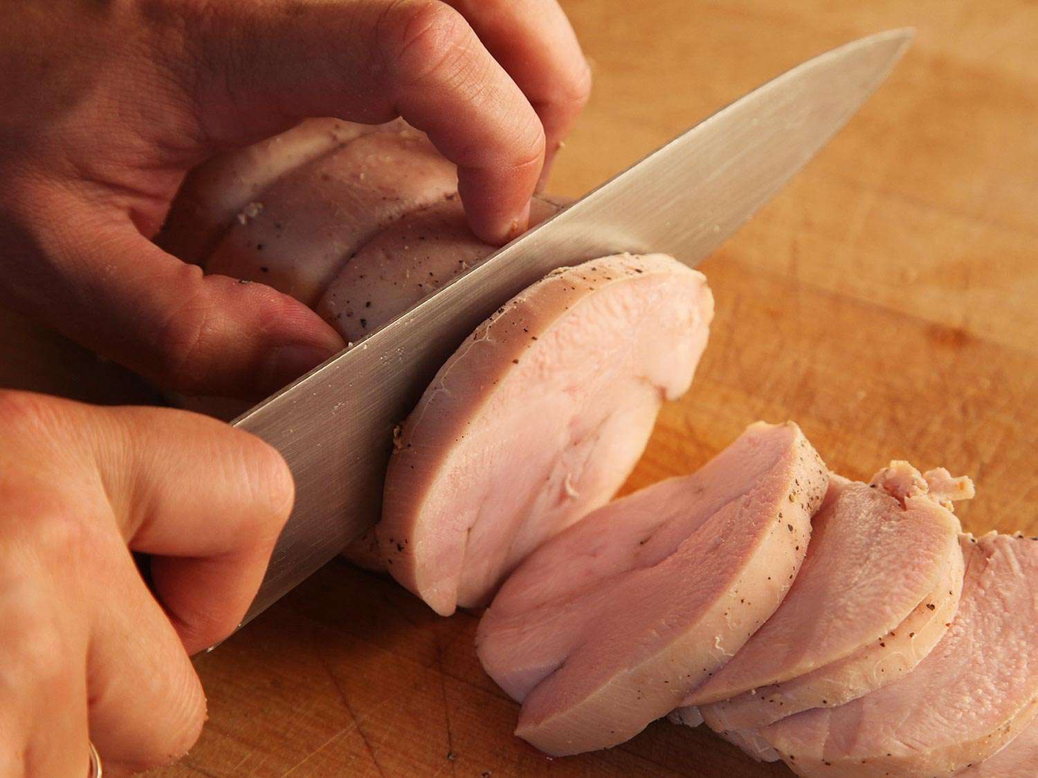 Slicing sous vide turkey breast on a wooden cutting board.
