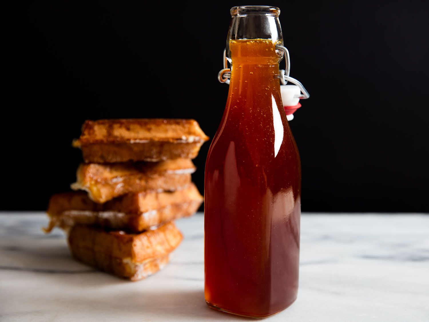 A bottle of homemade pancake syrup next to a stack of waffles.