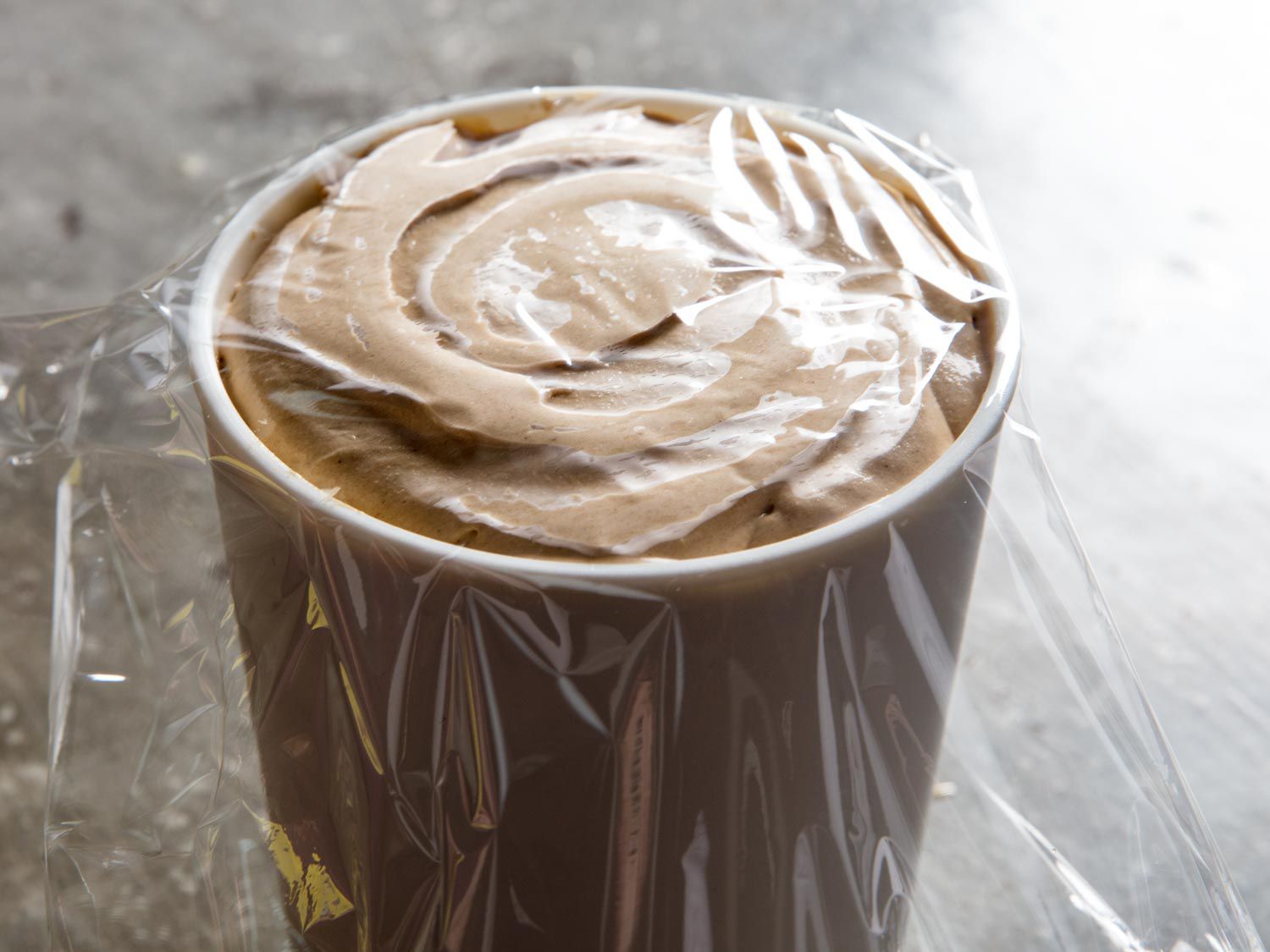 A piece of plastic wrap is placed over the surface of the ice cream.