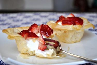 Two Greek yogurt and strawberry phyllo cups, served on a small plate. One has been partially demolished with a fork to reveal the yogurt filling.