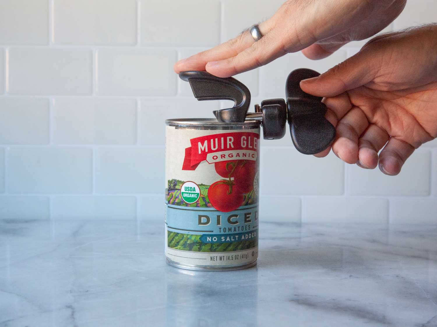 A person using a safety can opener to open a can of tomatoes