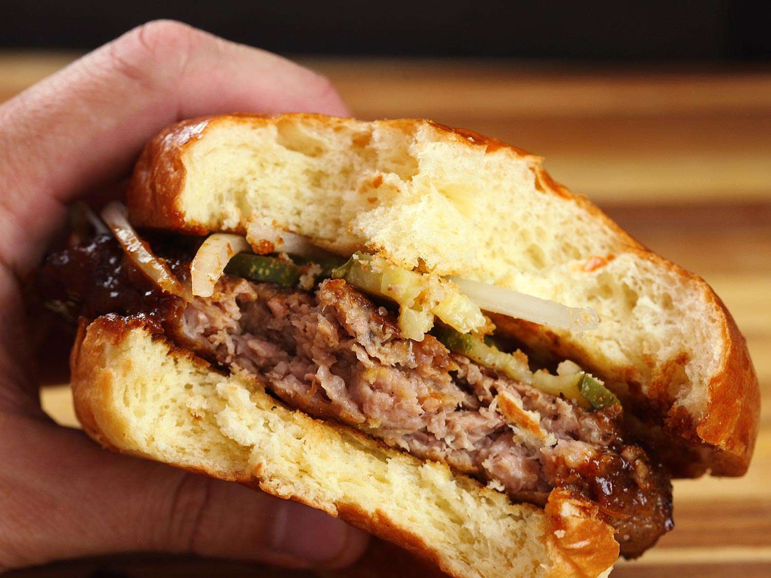 A partially eaten homemade rib sandwich topped with pickles and onions, held in a hand.