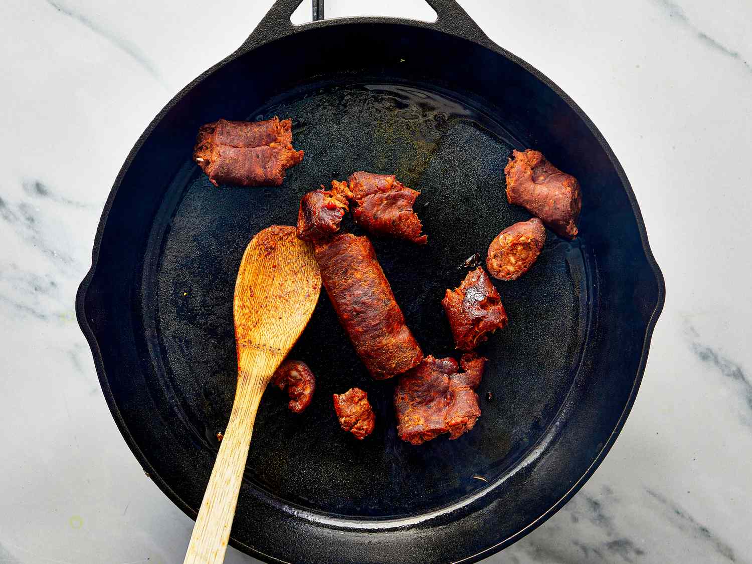 Cooking chorizo in a castiron skillet with a wooden spoon