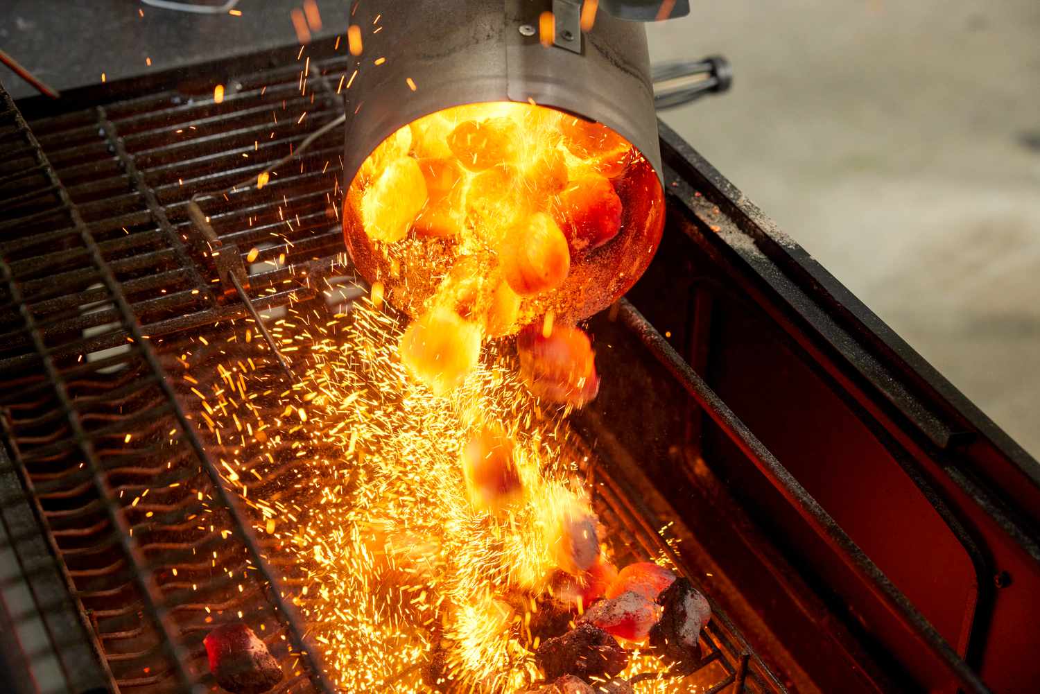 Charcoal being poured into a charcoal grill from a chimney starter.