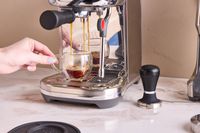 Espresso being brewed into a cup. A tamper is beside the espresso machine.