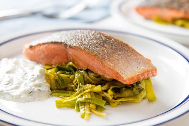 One-skillet salmon with curried leeks and yogurt-herb sauce, served on a white, blue-rimmed plate.