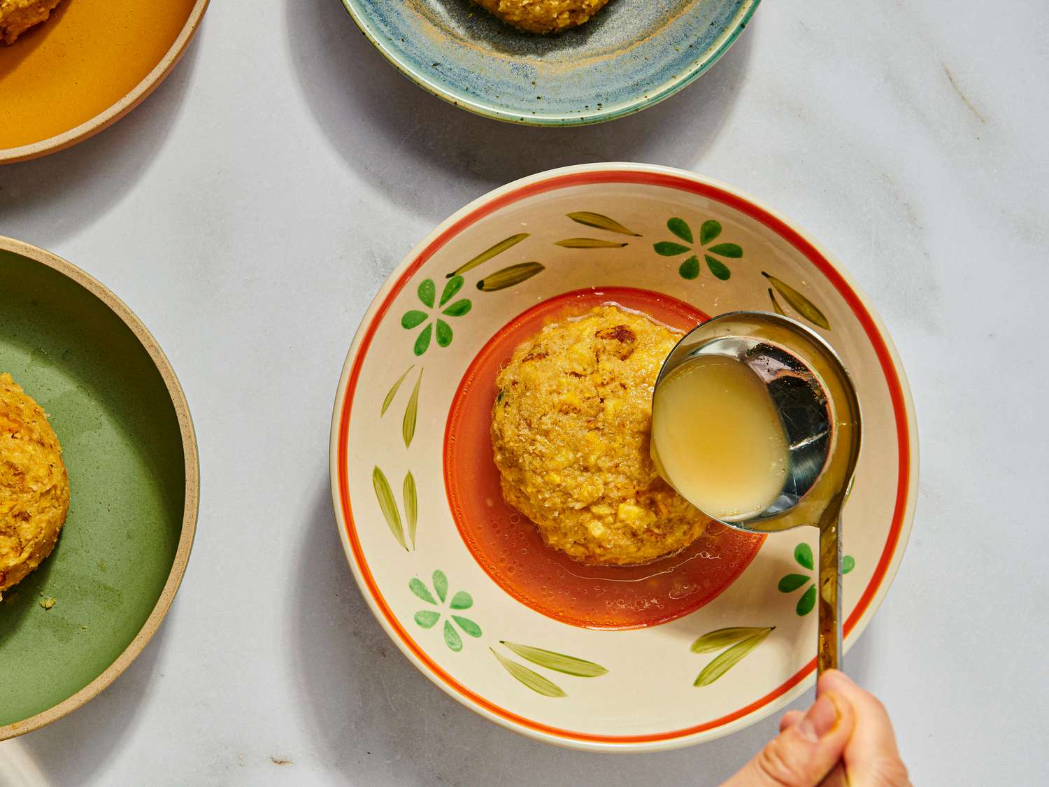 Ladling broth over mofongo on a bone colored flower print dish. 