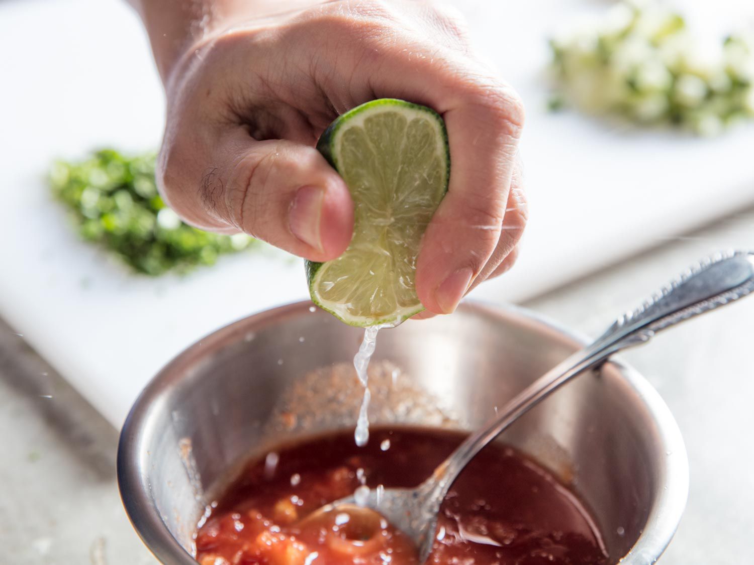 A lime half is squeezed over a bowl of salsa.
