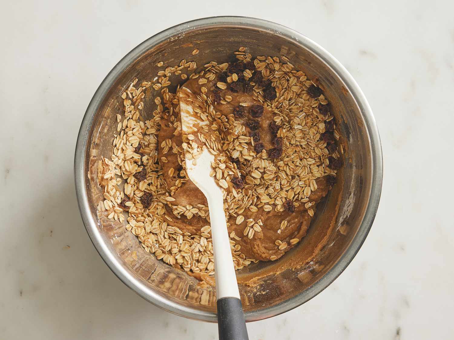 Folding raisins and toasted oats together in a metal bowl
