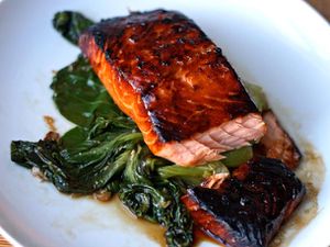 Teriyaki-glazed salmon on a bed of wilted bok choy on a white serving dish.