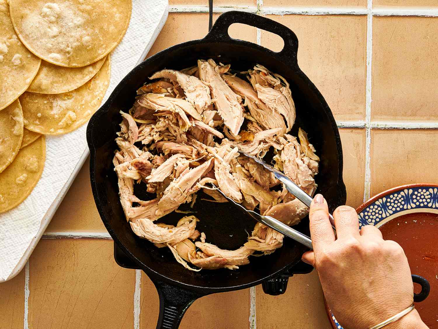 Pulled meat being shredded in a skillet with tortillas on the side