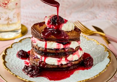 Stack of pancakes layered with cream and topped with berry sauce on a decorative plate