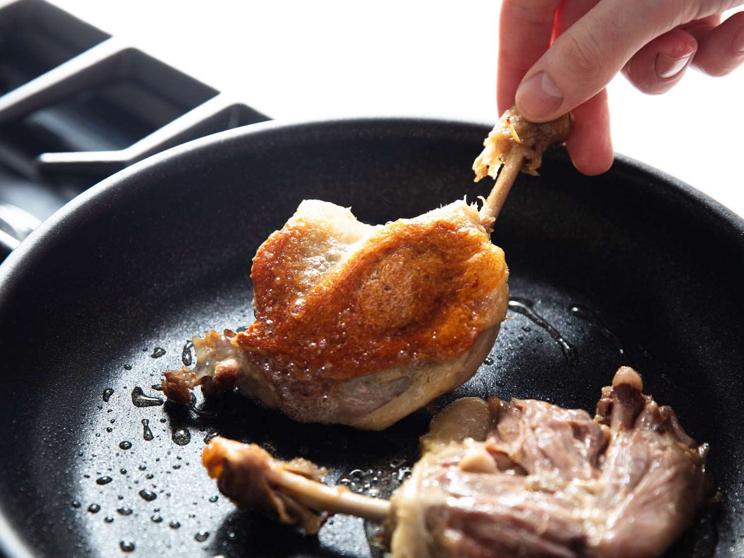 Turning confit duck legs over from skin side in a nonstick skillet.