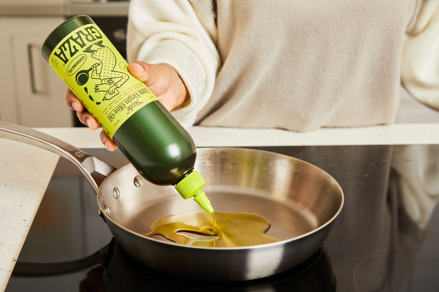 A person squirting olive oil into a skillet.