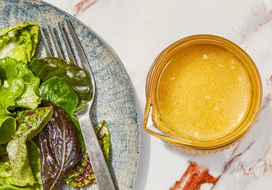Lemon vinaigrette in a small bowl next to a plate of greens.