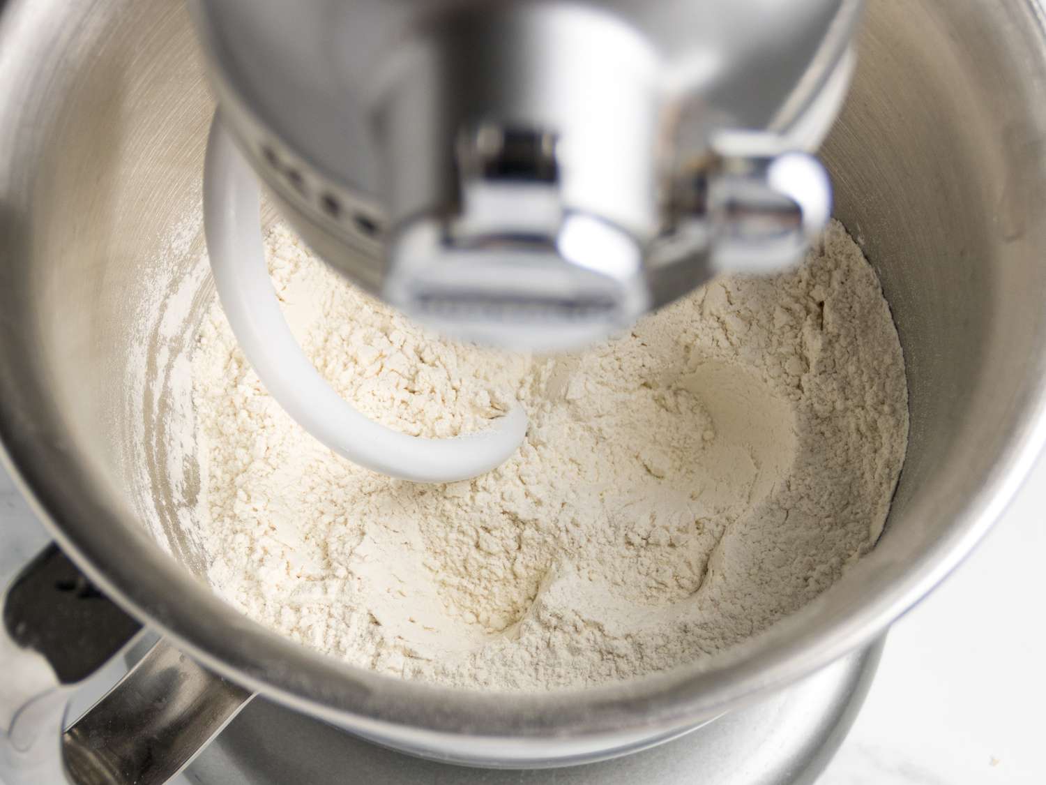 Flour in a stand mixer bowl with a dough hook attachment