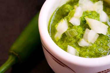 A ramekin of serrano salsa verde with diced white onion on top. 