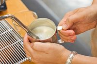 A close-up of a person's hands steaming milk with the Lelit MaraX Espresso Machine PL62X-120