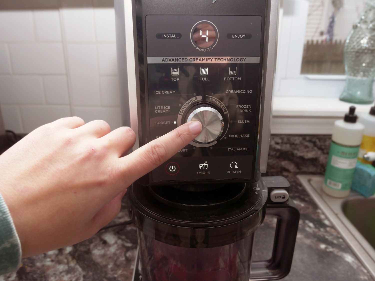 finger pressing the start button on the creami