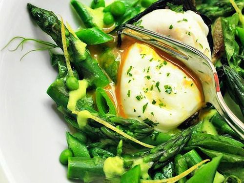 A closeup of a spring salad with a fork breaking open the yolk of a poached egg.
