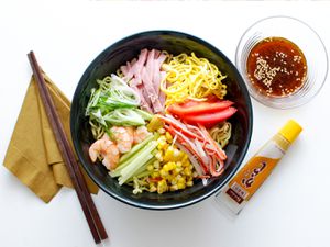Overhead view of hiyashi chuka, served in a black bowl with toppings artfully arranged like spokes on a wheel.