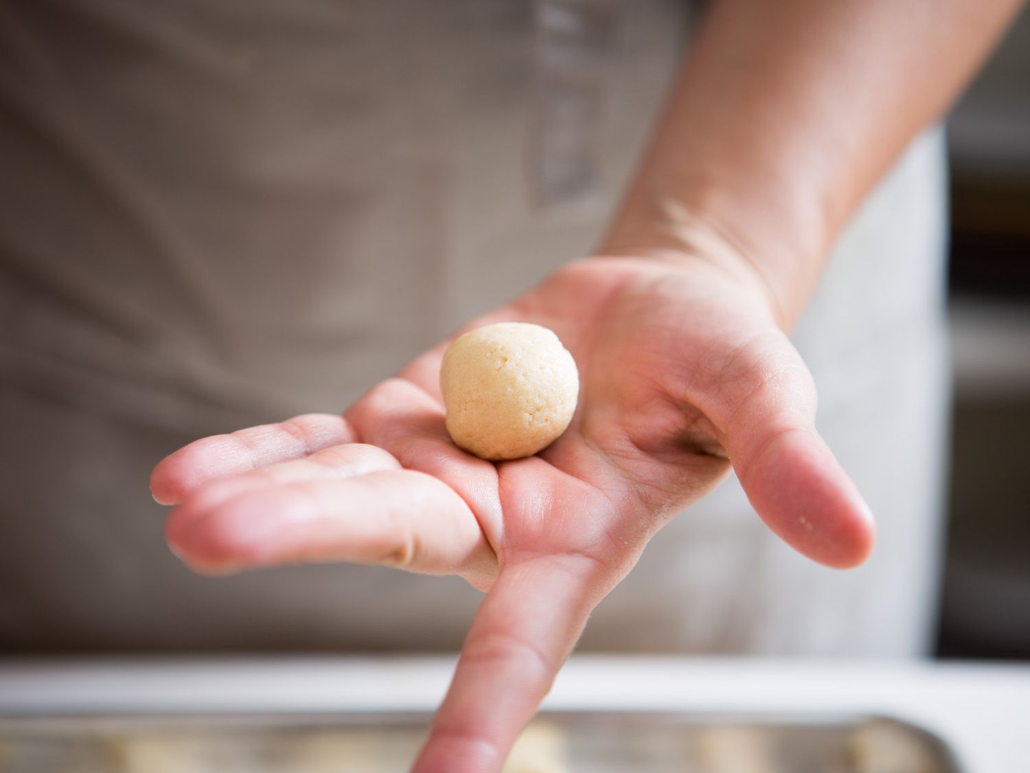 A hand holding a ball of rolled cookie dough.