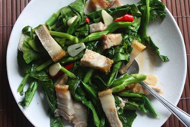Overhead view of stir-fried Chinese broccoli with crispy pork belly served on a white plate.