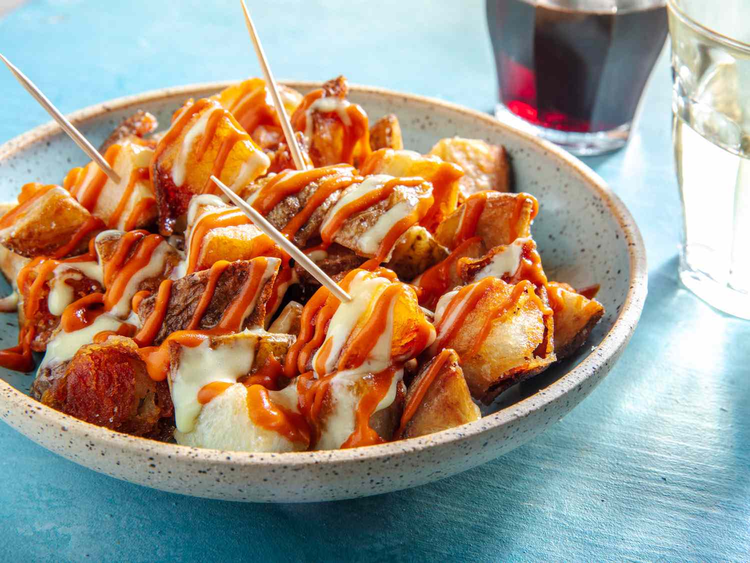 A small serving plate of patatas bravas drizzled with salsa brava and allioli