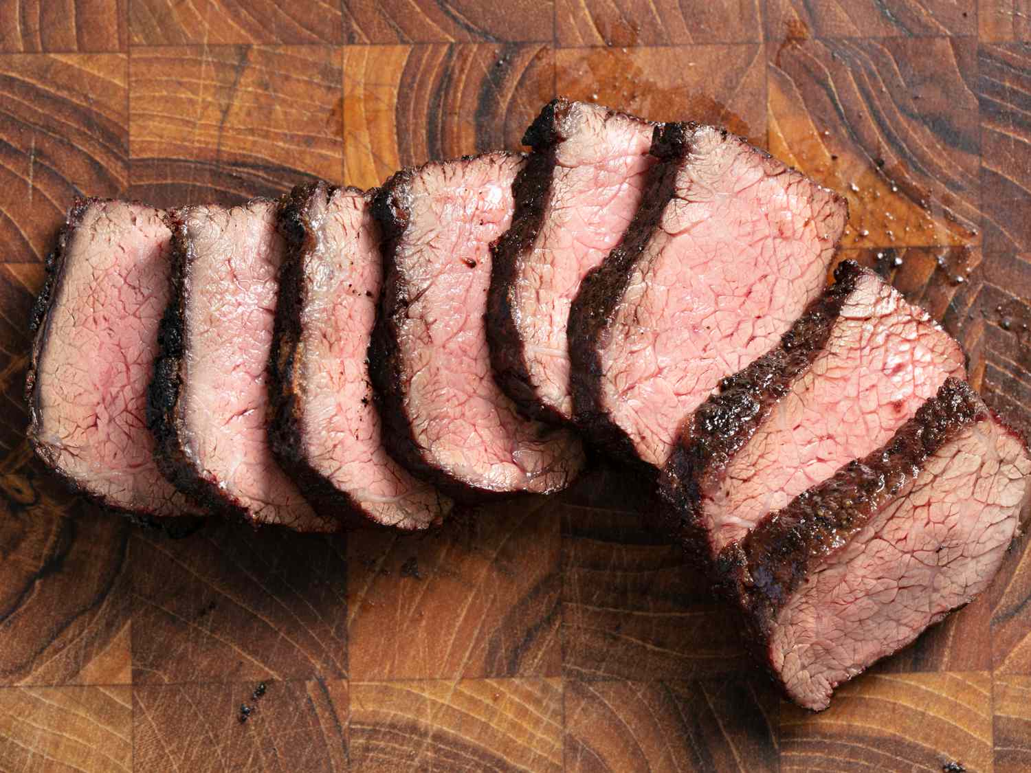 Grilled short rib sliced against the grain and spread out like fallen dominos on a cutting board.