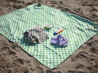 nomadix picnic blanket on the beach with a towel, popcorn, sunscreen, and sandals