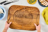 Hands holding a Lipper International Acacia Cutting Board with Grid Grip on a light countertop with utensils and food ingredients nearby