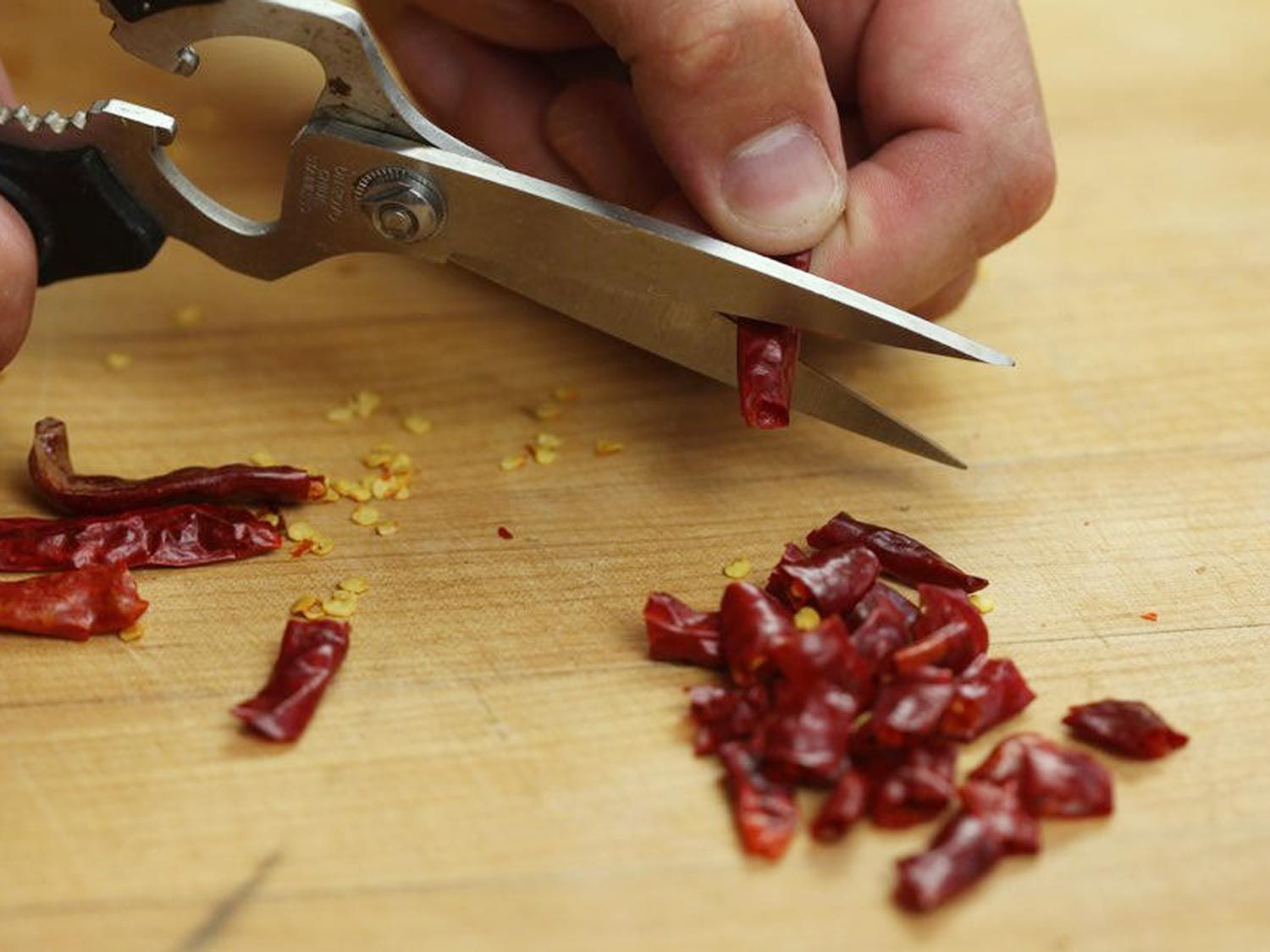 Cutting small dried red chiles into small pieces with scissors.
