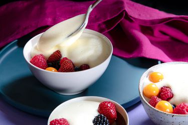 Zabaglione being spooned into a bowl of fruit with two other topped bowls in the foreground.