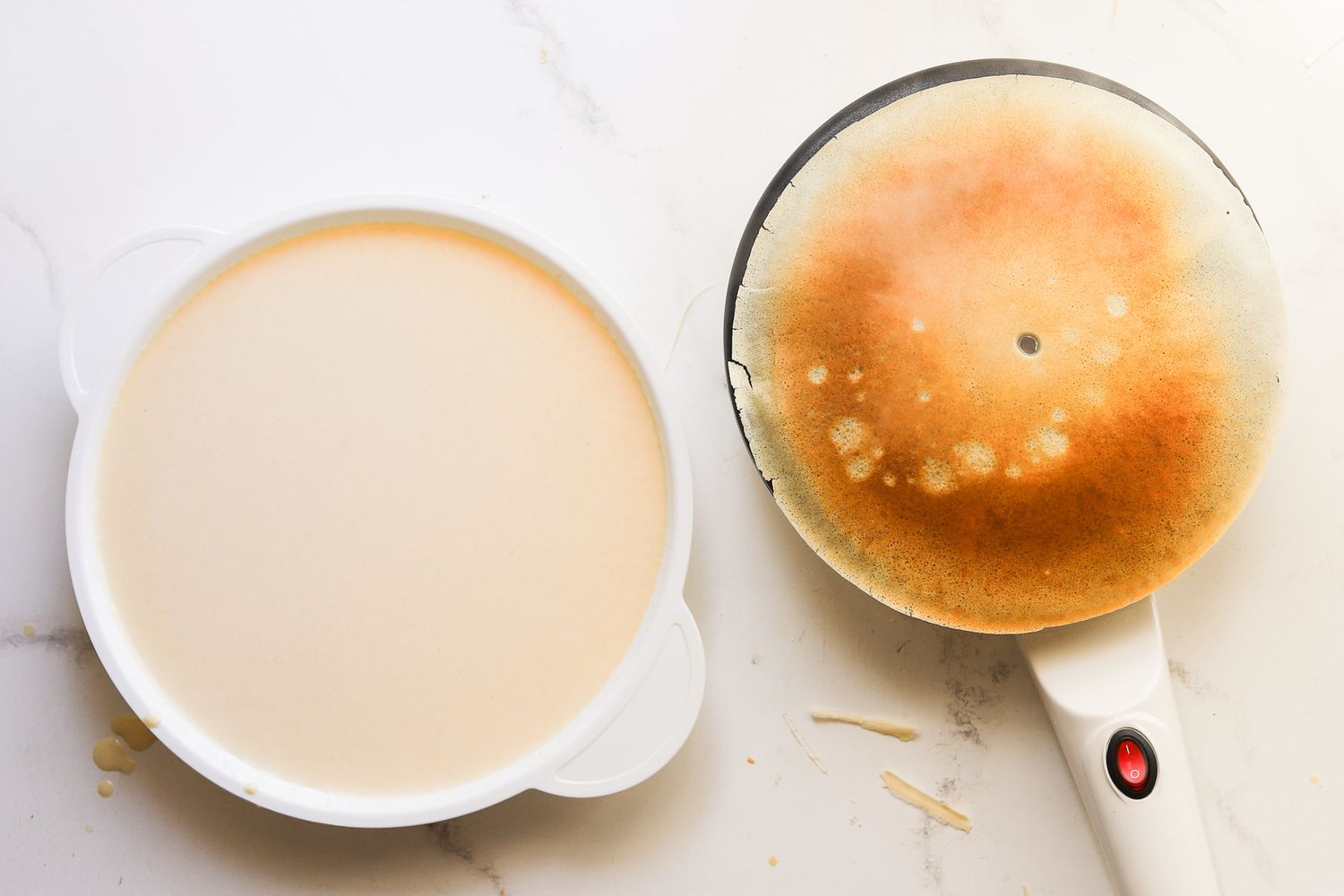 An electric crepe maker beside a bowl of batter.