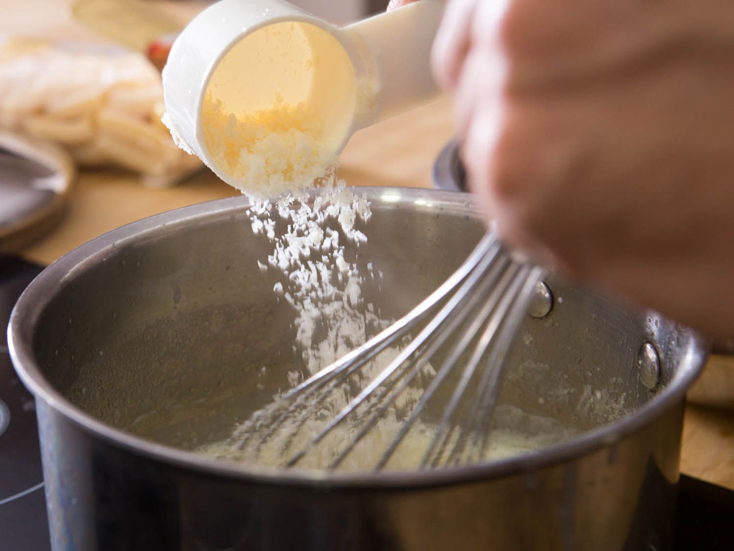 Sprinkling grated parmesan into a pot of cream sauce.