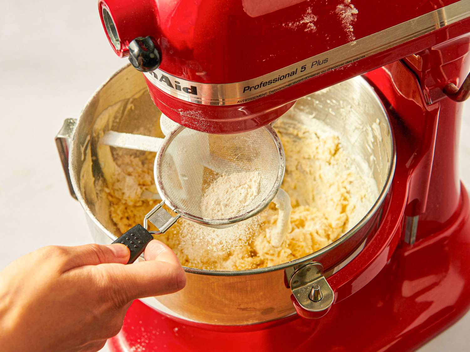 Mixing dough with a stand mixer flour being sifted in using a hand sieve